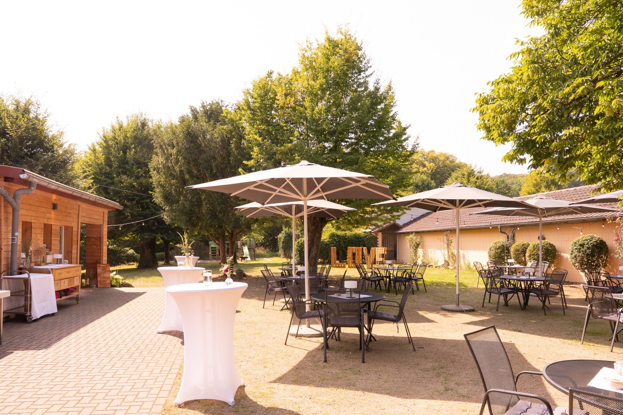 Biergarten mit Sitzplätzen, Sonnenschirmen und Stehtischen